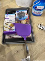 Metal baking sheet, purple silicone spatula, baking cookie press box, black heart-shaped cookie cutters partially visible inside tray