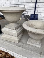 Two concrete planters side by side, one larger with stacked pedestal bases, one smaller.