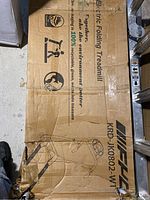 Photo of the top of the box showing model number KRD-JK0802-WT and images and logos including 'Electric Folding Treadmill'.
