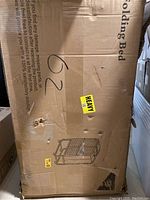 Photo of the cardboard box showing the folded bed frame illustration and 'HEAVY' sticker, box is somewhat worn with small holes