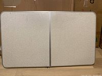 Top view of the folding table showing white textured surface and metal frame edges.