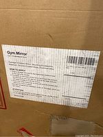 Close-up of the label displaying product name Gym Mirror 48x24-2pcs, packaging details, materials (silver-coated glass and aluminum alloy), and how to apply the mirrors on the wall.