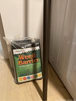 Packaged Usonhoo Weed Barrier landscape fabric wrapped in plastic, placed upright on floor next to white walls and door.