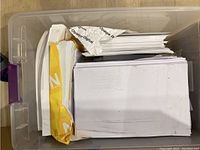 Clear plastic bin filled with assorted used printer paper sheets, some in partial branded packaging.