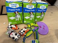 Full overview of all items: three packs of puppy pads and seven assorted new dog toys including squeaky bones, a star-shaped toy, frisbee, and rope toy.