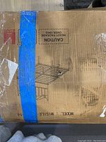 Cardboard box showing sketch of queen metal bed frame and headboard, taped with blue painter's tape