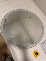 Top view of the round vanity mirror showing the reflective surface protected by plastic film with three orange securing dots on its surface.