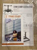 Photo of instruction manual and parts list for Stand Steady Electric Desk model DMME2BL/DMME3BL in plastic packaging.