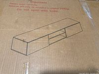 Illustration of the TV stand design on the box, showing long rectangular shape with two closed storage units on each side and two open shelves in the middle.