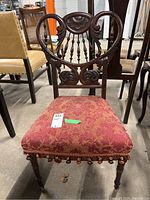 Front view of antique occasional chair showing red upholstered seat, carved wooden frame and front casters.