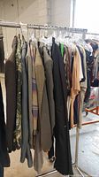 Side view of clothing rack with men's blazers and other assorted clothes hanging on hangers.
