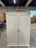 Front view of closed white painted cabinet with two paneled doors and metal knob handles.