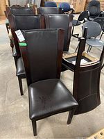 Six matching brown PVC leather upholstered and wood framed dining chairs seen from the front and side views. One chair is shown turned upside down with visible frame nicks.