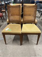Two matching wood chairs with cane backs and upholstered seats, showing wear and some damage on the cane backs and seat fabric
