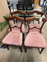 Front view of four vintage wooden chairs with pink upholstered seats and carved backrests, showing wear and some stains.