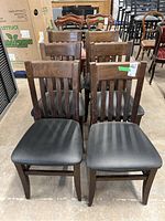 Front view of six wooden frame chairs with black upholstered seats arranged in two rows.