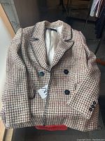 Zara women's blazer laid out showing double-breasted front, cream and black tweed-like fabric with black buttons.