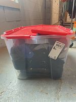 Full view of plastic tote bin with red lid containing socks, shoes, and other clothing items