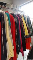 Photo showing various tops, shirts, blazers, and jackets hung on a clothing rack in different colors and patterns.
