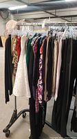 Photo displaying a rack of assorted women's clothing items including dresses, pants, shirts, scarves, and a blazer.
