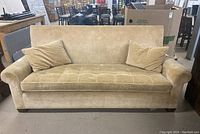 Front view of beige upholstered sofa with two cushions on each end, tufted seat cushion, and rounded armrests.