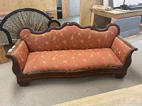 Front view of wooden framed couch showing red floral upholstery and scalloped top backrest.