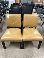 Front and rear view of two matching Ethan Allen chairs with tan leather upholstery and dark wood frames, showing wear and nailhead stud trim.