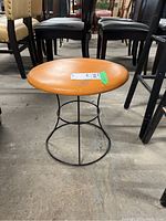 Full view of Mid-Century Modern vinyl upholstered stool with wire base, positioned on concrete floor among other chairs and furniture.
