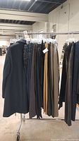 Full shot of rack with Zara men's black coat and 9 pairs of men's pants including jeans, corduroy, khaki, and dress pants.