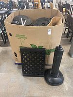 Cardboard box with plastic lattice panels, large round black plastic bases, and some metal poles visible around the box.