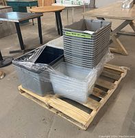Pallet of plastic storage bins wrapped in plastic showing gray, dark blue, and translucent white bins stacked and nested.