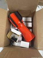 Photo of the orange retractable rope barrier housing with multiple small white boxes inside a cardboard box.