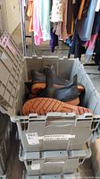 Bin of multiple black rubber shoes with brown soles stacked inside a grey plastic bin, sizes 11-13 indicated on label.