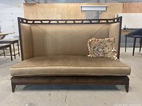 Front view of beige settee style couch with wooden lattice top and one decorative floral pillow.