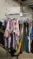 Rack of multiple women's tops, t-shirts, tank tops in assorted colors and sizes hung on plastic hangers with some tags visible.