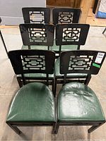 Six Stakmore folding chairs arranged in two rows, showing green faux leather seats and black painted wood backs with geometric cutouts.