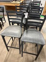 Set of four metal framed high stool chairs with gray upholstered seats, arranged in a group. Two front chairs show the upholstery condition clearly with some tears visible on two seats. The stools have a 29 inch seat height and metal ladder backs with horizontal slats.