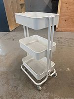 Front-right angled view of white 3-tier metal utility cart on casters showing structure and design.