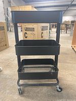 Front view of a black metal utility cart with three tiers and caster wheels.