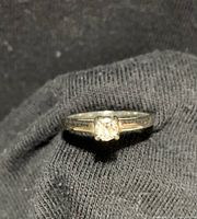 Front view of ring on black fabric showing round center diamond in solitaire setting