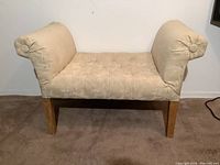 Front-left angle view showing beige upholstery, floral pattern, rolled armrest with decorative tuft button, button tufting on seat, and wooden legs.