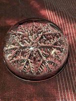 Clear vintage crystal paperweight showing intricate snowflake design inside with textured branches and air bubbles, viewed at an angle on a dark fabric background.