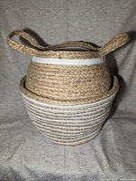 Two stacked natural jute storage baskets with woven handles and white stripes on a fabric surface.