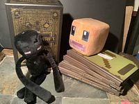 Black Enderman plush, orange Steve head plush, several Minecraft hardcover guidebooks stacked, and Minecraft collectible box.