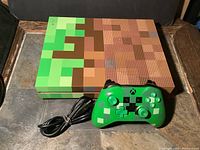 Xbox One S Minecraft Edition console with pixelated Minecraft block design and green pixelated Xbox controller with power cable