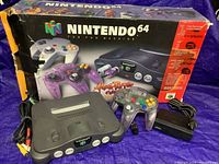 Nintendo 64 console with controller and accessories in front of original box, showing packaging condition and contents.