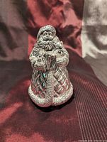 Front view of silver-tone Santa Claus musical ornament showing detailed quilted coat and presents held in hands.