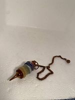 Photo showing entire vintage pendant with multi-layered colored stones and attached copper/bronze chain, on white surface.