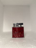 Front view of the vintage red metal lighter with chrome ignition top and decorative line design.