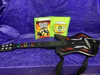 Xbox 360 Guitar Hero World Tour guitar controller laid out flat with game case and disc open behind it.